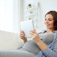 Schwangere Frau liegt auf dem Sofa und informiert sich